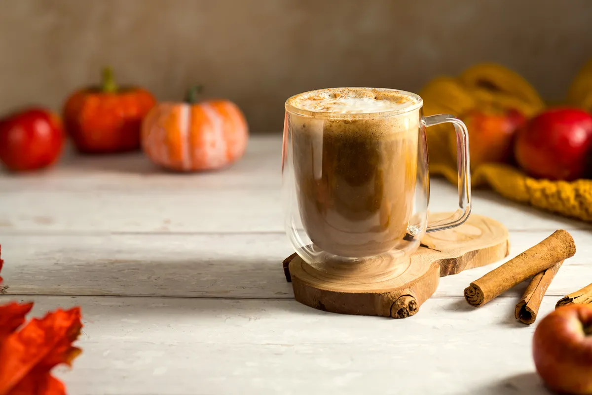 Pumpkin spice latte fehér asztallapon almával, sütőtökkel, fahéjrúddal és levelekkel. 