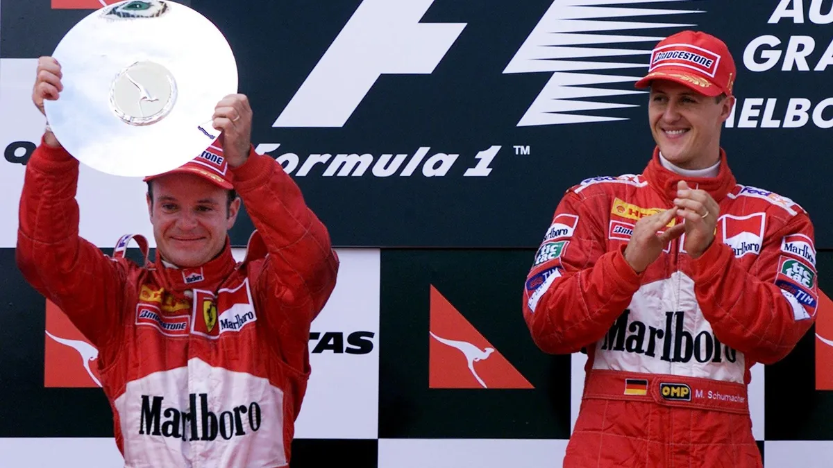 Ferrary driver Rubens Barrichello (L) of Brasil displays his trophy for second place as teammate and former two-time world champion Michael Schumacher (R) of Germany applauds on the podium of the Australian Formula One Grand Prix in Melbourne, 12 March 2000.  Michael Schumacher won the first race of the season with a time of 1:34:01.987 - 11.415 seconds ahead of Barrichello.  (ELECTRONIC IMAGE)  AFP PHOTO/Torsten BLACKWOOD (Photo by TORSTEN BLACKWOOD / AFP)