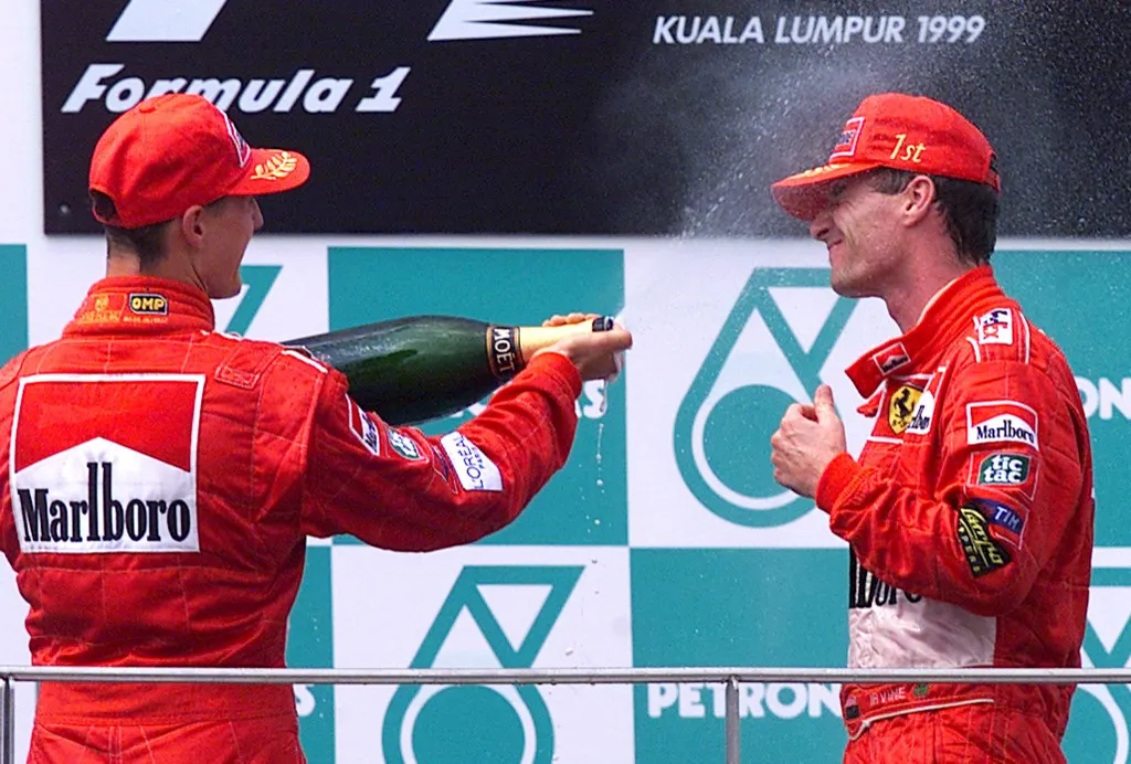 Ferrari team Formula One driver Eddie Irvine of Northern Ireland (R) is sprayed with champagne by teammate Michael Schumacher of Germany 17 October 1999 on the victory podium of the Malaysian Grand Prix in Sepang. Irvine won the race ahead of Schumacher after Schumacher let Irvine overtake him to allow him to take the lead in the drivers' World Championship. (ELECTRONIC IMAGE) AFP PHOTO/Emmanuel DUNAND (Photo by Emmanuel DUNAND / AFP)